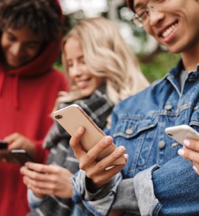 A group of diverse students looking at smartphones and smiling